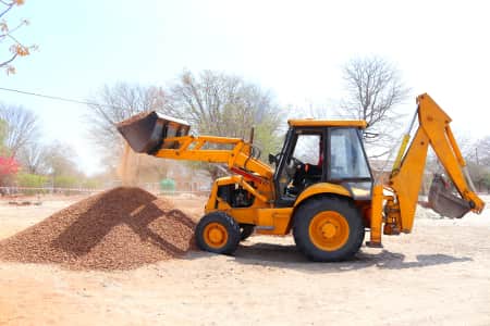 Backhoe loader lifting load of dirt on construction site